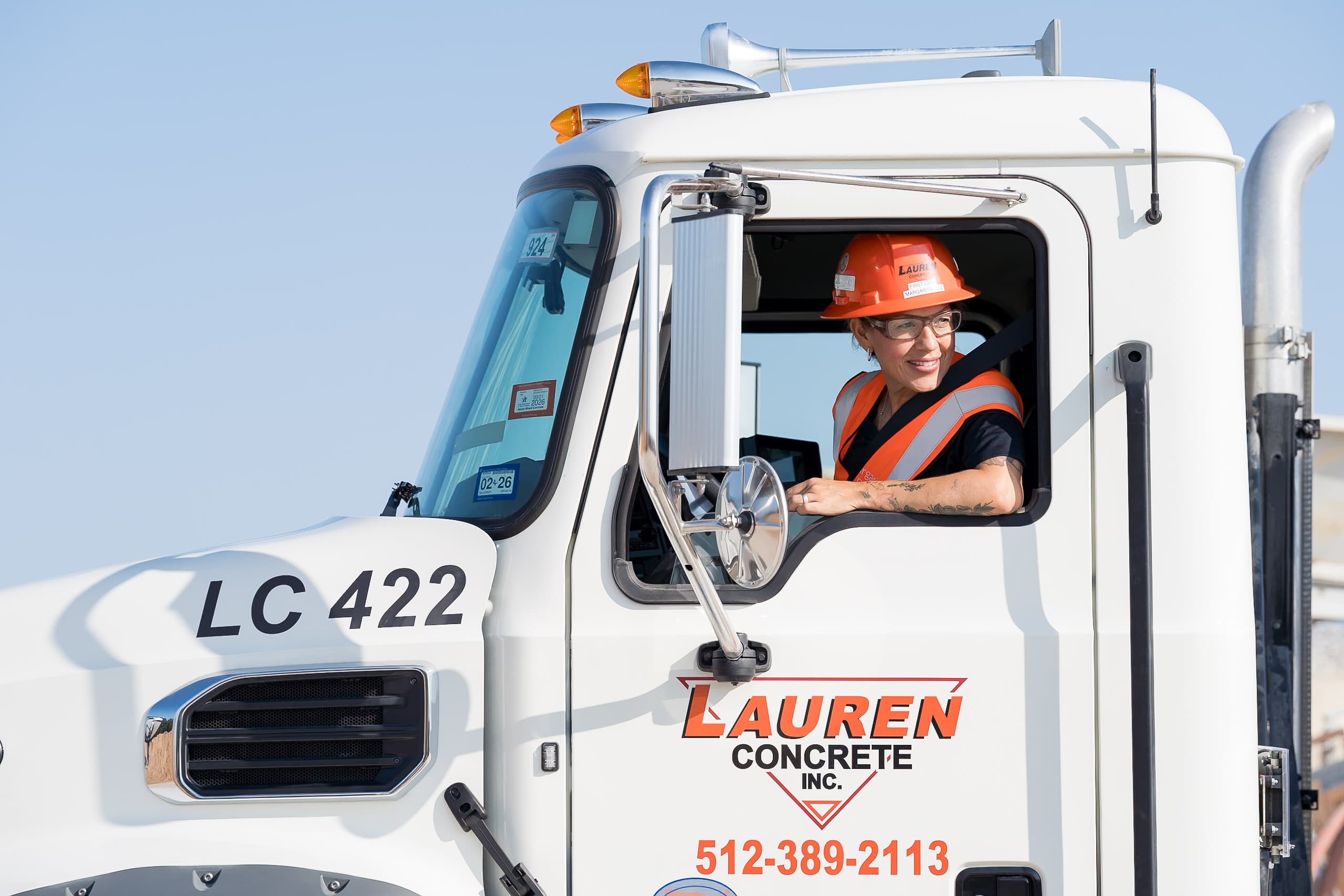 A picture of a woman driver, backing up a lauren concrete ready-mix truck and looking out the window and smiling