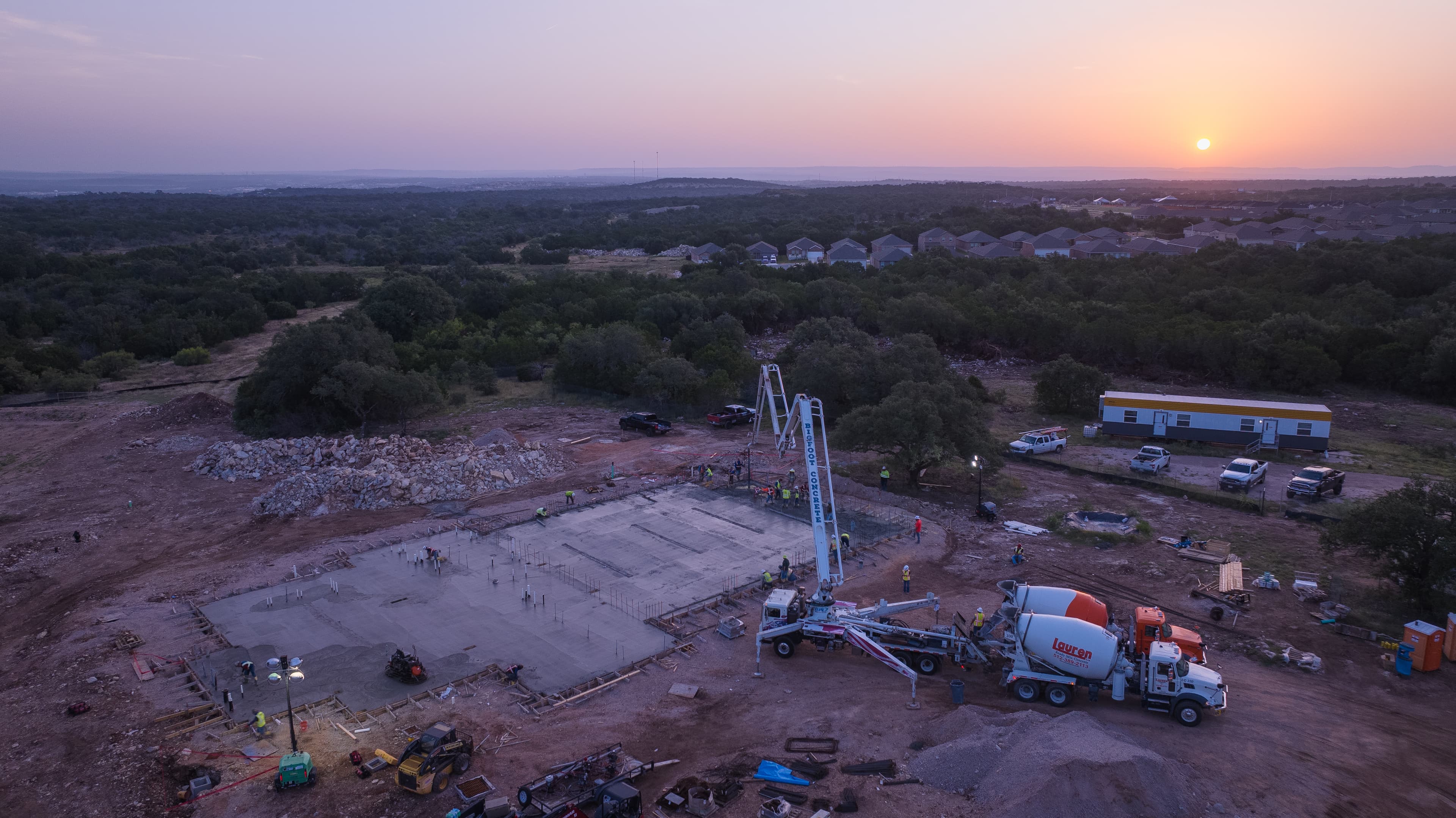 Sun rising over a freshly placed concrete slab with a pump truck and mixer trucks in the shot