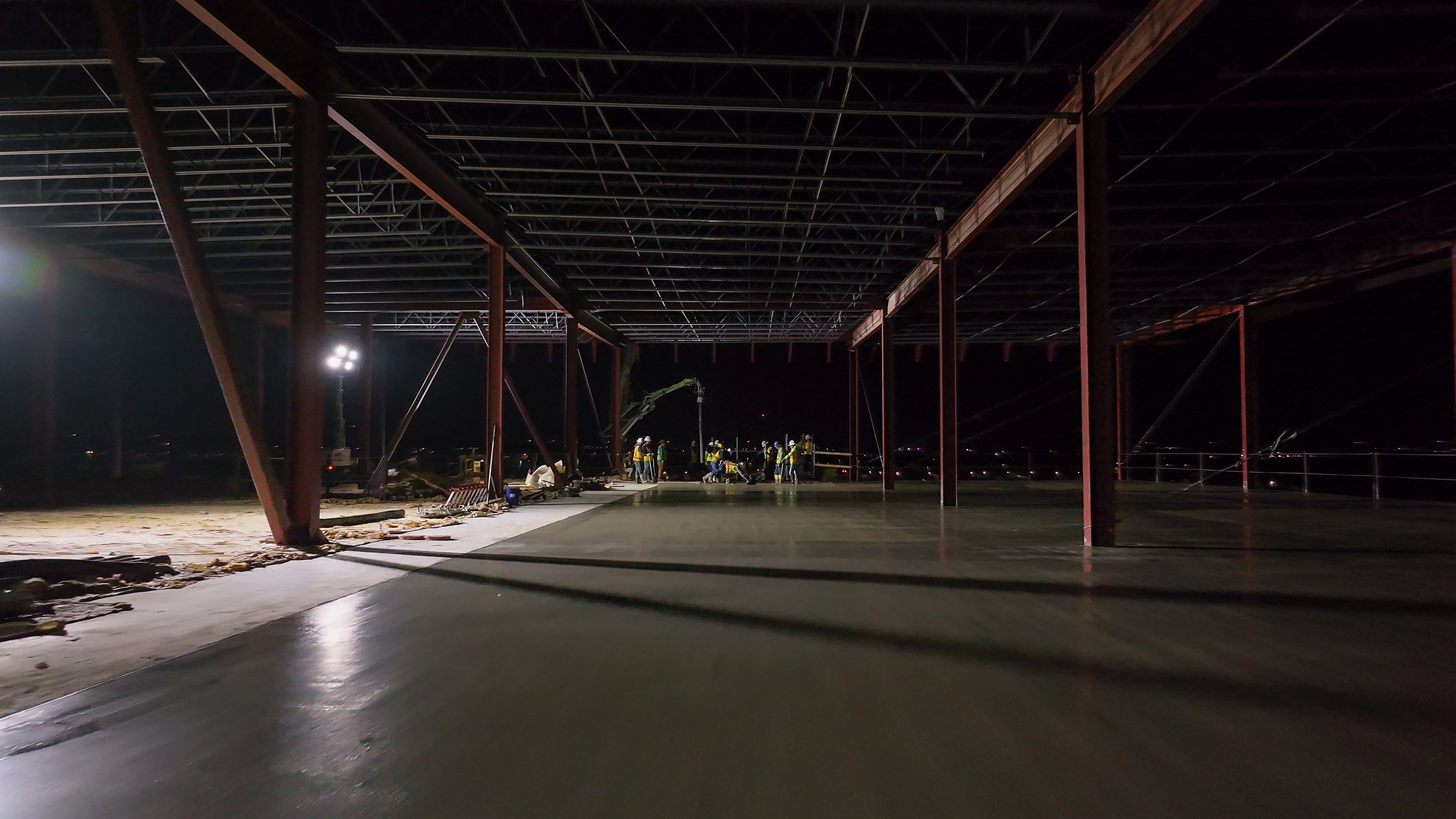 freshly poured concrete smoothed out with a finishing crew and pump in the background